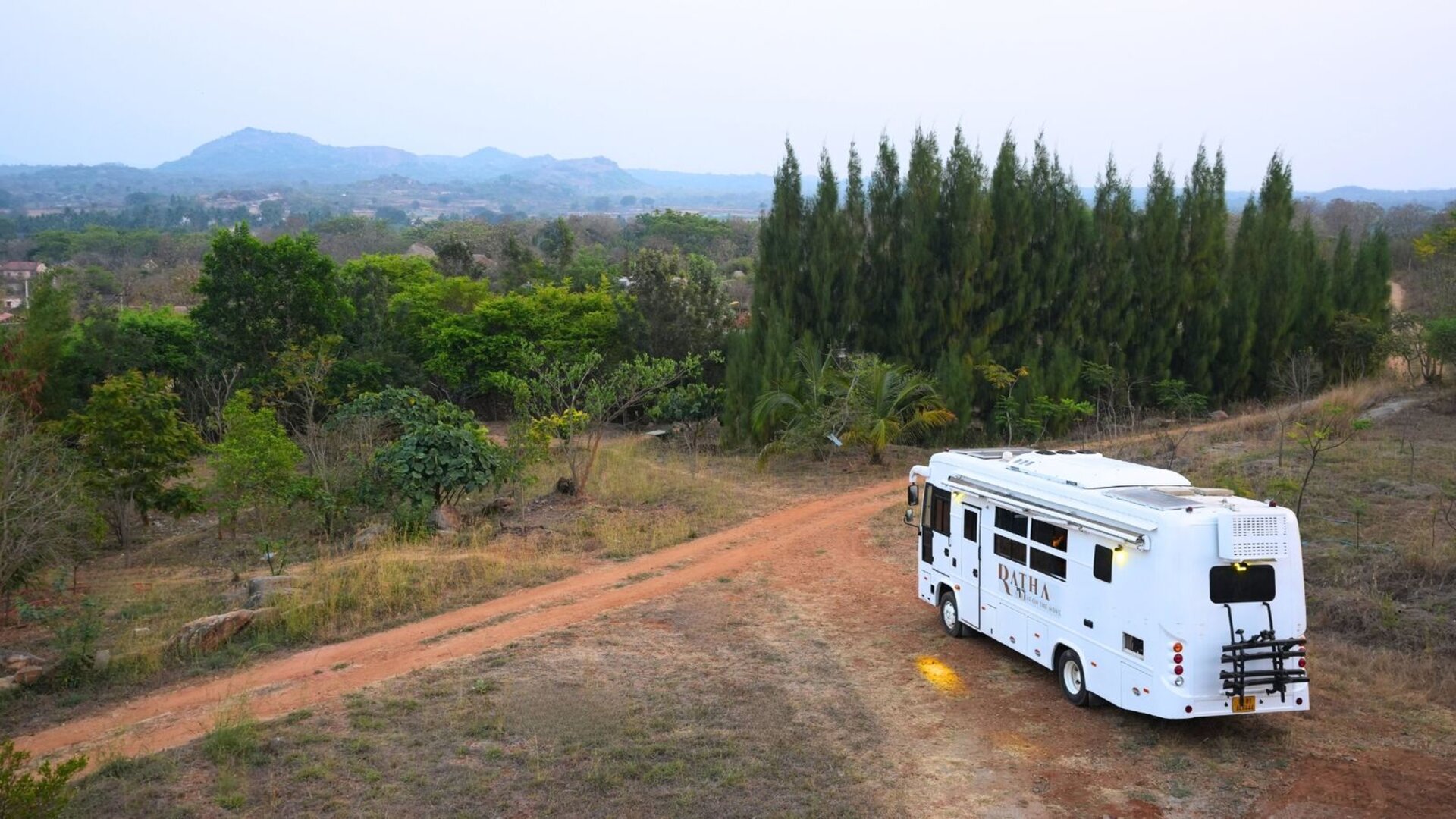 Ratha luxury caravan for rent in Bangalore — drone top view of White Caravan amid trees and open landscape
